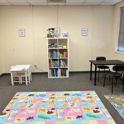 Speech Bloom - Therapy room with floor play area mat, bookshelf with therapy materials and seating for younger and older children.