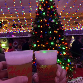 Happy's: A Holiday Bar - two people holding beer glasses in front of a christmas tree - Cocktail Bars Near Me - Chicago, Illinois Happy's: A Holiday Bar - two people holding beer glasses in front of a christmas tree - Cocktail Bars Near Me - Chicago, Illinois