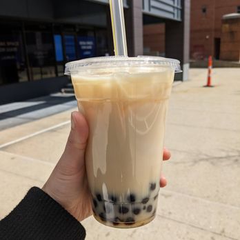 Dado Tea - Large bubble tea - A person holds a large plastic cup of bubble tea with tapioca pearls at the bottom, outdoors near a modern building. - Bubble Tea Near Me - Cambridge, Massachusetts