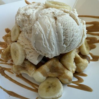 Wondaffle - A dessert with a scoop of vanilla ice cream placed on banana slices and waffle pieces, drizzled with caramel sauce, served in a paper dish. The presentation includes banana slices scattered around the waffle and caramel decoration on the plate. - Waffles Near Me - Bethlehem, Pennsylvania