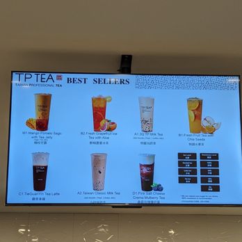 TP Tea - The image shows a digital menu board at TP Tea in Nepean, ON, featuring a selection of best-selling tea drinks. The menu includes mango pomelo, fresh grapefruit ice with aloe, milk tea, fruit tea with chia seeds, tea latte, classic milk tea, and salted cheese tea. The display also shows a beverage temperature and sweetness level chart. The background includes a white tiled wall and a refrigerator below the menu with various drinks inside. - Donuts Near Me - Nepean, Ontario