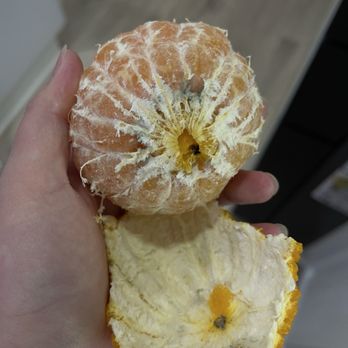 Amazon Fresh - A person holds a peeled orange and a partially peeled orange in their hand, with a blurred indoor background. - Grocery Near Me - Fullerton, California