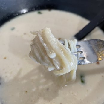 Fun Noodle Bar - Undercooked noodles. Clumped together, chewy, yucky. - A close-up of a fork holding noodles in a creamy soup, with a black bowl and a spoon visible in the background. - Chinese Near Me - Santa Fe, New Mexico
