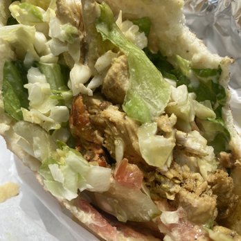 Beyond Pita - Chicken shawarma pita - A close-up image of a chicken shawarma pita sandwich showing shredded lettuce, chopped vegetables, and grilled chicken pieces inside a pita bread. The pita is partially open, revealing the filling, and the background includes aluminum foil. The sandwich appears freshly prepared, with a variety of textures and colors from the vegetables and meat. - Mediterranean Near Me - Montclair, New Jersey