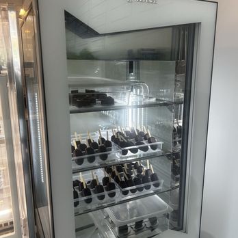 Frera - A glass-front refrigerated display case contains multiple trays of chocolate-covered ice cream bars on sticks, arranged in rows. - Coffee & Tea Near Me - Chicago, Illinois