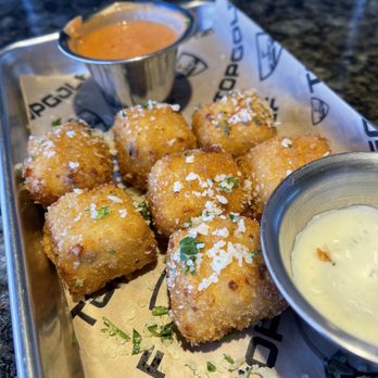 Topgolf - Cheesy Macaroni Bites - A metal tray holds fried cheese balls garnished with grated cheese and herbs, accompanied by two dipping sauces, one orange and one white. - New American Near Me - Albuquerque, New Mexico