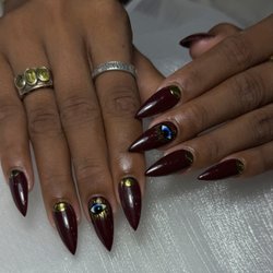 Magic Nails - Burgundy almond nails with gold accents and hand-painted evil eye nail art at Magic Nails in Buena Park, CA.