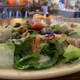 Greek Salad - A Greek salad featuring lettuce, tomatoes, cucumbers, olives, shredded carrots, and feta cheese served on a white plate.