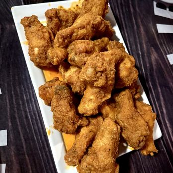 Tipsy McStaggers - Classic Plain Wings (20) tossed in Buffalo sauce. - A rectangular white plate holds several pieces of fried chicken wings, which are golden-brown and crispy. The wings are placed on a dark wooden table, with part of a white plate visible in the top right corner. The image captures the texture and color of the fried chicken, emphasizing its crispy coating. - Bars Near Me - Warren, Michigan