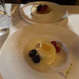 Panna cotta - A panna cotta dessert topped with citrus jelly and surrounded by blackberries and raspberries, served on a white plate.