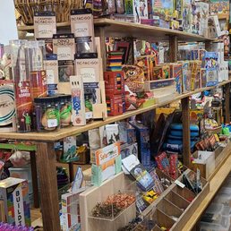 Toys toys TOYS! - A toy and gift shop displays shelves stocked with board games, craft supplies, and small toys, with organized containers and a wicker basket on top.