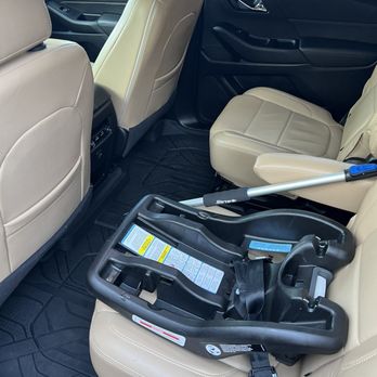 TMD Auto Detailing - Interior detail - A beige child car seat base is secured on the rear passenger seat of a vehicle with black interior, with a cleaning tool resting on it. - Auto Detailing Near Me