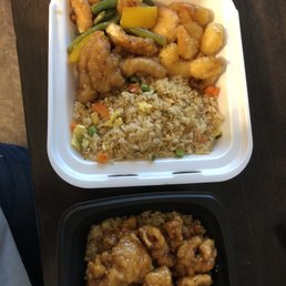 Orange Chicken - Two takeout containers of Chinese cuisine, featuring fried rice with vegetables, orange chicken, and honey walnut shrimp, on a dark wooden surface.