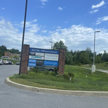 Labcorp - Entrance - The image shows a roadside sign mounted between two brick pillars on a grassy median, indicating the location of medical facilities including LabCorp and Geisinger on 521 Mt. Pleasant Drive. The sign lists services such as clinical nutrition, obstetrics, gynecology, weight management, and metabolic surgery. In the background, there is a parking lot with several cars, a building, and a partly cloudy sky with some trees and streetlights visible. The scene appears to be in a commercial area with accessible parking and clear signage. - Laboratory Testing Near Me - Scranton, Pennsylvania