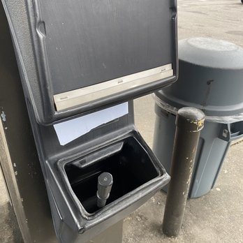 RaceWay - The image depicts an outdoor parking lot pay station with a black card reader and a small empty compartment below it. A gray trash bin is positioned next to the station, and a black bollard is nearby. In the background, several parked cars and a building with multiple units are visible, indicating a commercial or residential area. - Convenience Stores Near Me - Birmingham, Alabama