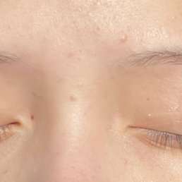 A close-up image of a person's face focusing on closed eyes, with visible eyebrows and eyelashes, taken in a setting related to eyebrow threading.