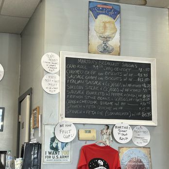 Martha's Diner - Inside Martha's Diner in Ellsworth, ME, a menu board lists breakfast specials, and signs advertise fruit cups and a T-shirt. A red T-shirt with the diner's logo hangs on the wall. - American Near Me - Ellsworth, Maine