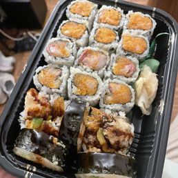 Shrimp Tempura - A black plastic sushi container holds assorted sushi rolls, including spicy yellowtail, tempura, and other varieties, with pickled ginger on the side.