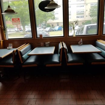 Woonsocket Palace Pizza - a view of the inside of a restaurant - A restaurant interior features booths with black seats and light-colored tabletops, positioned along large windows showing parked cars and buildings outside. - Pizza Near Me - Woonsocket, Rhode Island