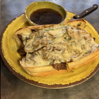 Saluti’s - Italian Beef Dip - A bread bowl contains a creamy mushroom and beef mixture, accompanied by a small bowl of dark gravy, on a yellow plate. - Italian Near Me - Jackson, California