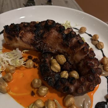 Ember & Cork - Octopus appetizer with crispy chick peas - A grilled octopus tentacle is presented on a white plate, garnished with chickpeas, sauce, and shredded vegetables, with decorative drizzles. - Seafood Near Me - Schenectady, New York