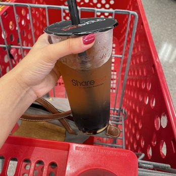 Sharetea - Boba is the new Starbs - A person with red painted nails is holding a large plastic cup of iced bubble tea with a black straw. The cup has a black plastic lid and the label 'Share' on it. The shopping cart is red with a metal frame, and the background shows store shelves and a gray floor. - Bubble Tea Near Me - St. Charles, Illinois