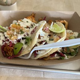 Street Tacos - Two street tacos filled with chicken, vegetables, and sauces, garnished with lime wedges, served on a tray with a plastic fork.