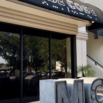 Morse Code Lounge - The image shows the storefront of Morse Code Lounge with a black awning displaying its name and large concrete letters 'M' and 'C' outside. - Wine Bars Near Me - Winter Park, Florida