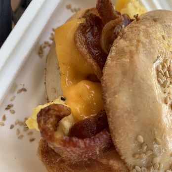 Hound and Mare - The OG with bacon - A breakfast sandwich featuring bacon, melted cheese, and scrambled egg on a sesame seed bun, served in a white takeout container. - Cafes Near Me - Ithaca, New York