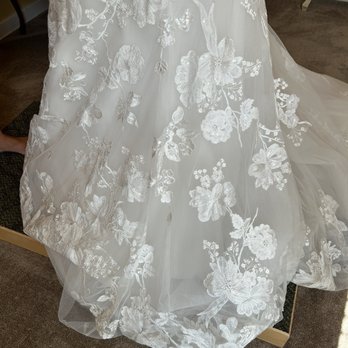 Something Blue Bridal - A wedding gown with floral embroidery on sheer fabric is shown, featuring intricate lace and embroidery details, displayed indoors. - Bridal Near Me - Schererville, Indiana