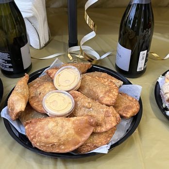 Sammy’s Subs - Can you say empanada?! - Plate of fried empanadas with dipping sauce, set on a table with wine bottles and gold ribbon decorations, indicating a celebration. - Sandwiches Near Me - Wayne, New Jersey