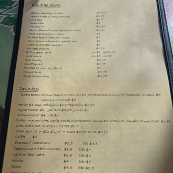 Tune-Up Cafe - Menu 2025 - The menu features sections for food and drinks, listing items such as bacon, sausage, eggs, home fries, and tortillas, with prices ranging from $2.5 to $6.95. The drinks section includes beers, sodas, juices, and coffee, with detailed options like Mexican Coke, Sprite, and various coffee beverages, along with their prices. The menu is printed on a light-colored paper and is placed on a dark frame, with a background of a green surface with floral patterns. - New Mexican Cuisine Near Me - Santa Fe, New Mexico