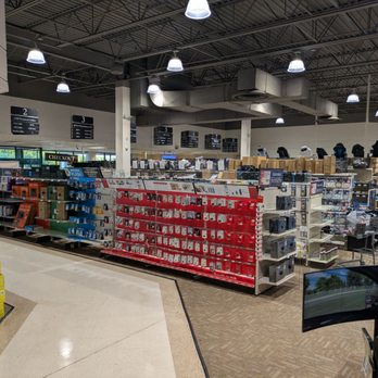 Micro Center - Interior - The image shows the interior of an electronics retail store with high ceilings and bright lighting. Shelves are filled with various electronic accessories, including camera equipment, cables, and other gadgets. Signage indicates checkout counters and product categories. The store layout includes multiple aisles and display sections, with shopping carts visible in the background. - Computers Near Me - St Davids, Pennsylvania