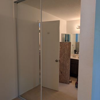 OC Fixit - OC Fixit Installed ceiling-to-floor mirrored closet doors - A sliding mirrored closet door is partially open, showing a view into a bedroom with a bathroom and a door. - Furniture Assembly Near Me