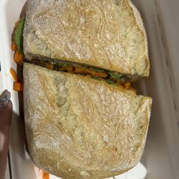 Breakfast Banh Mi - A sandwich with bread, shredded carrots, and leafy greens inside a white takeout container.
