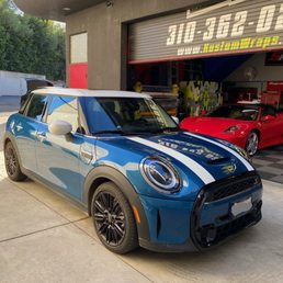 Blue Mini Cooper with white roof, mirror caps, and racing stripes.