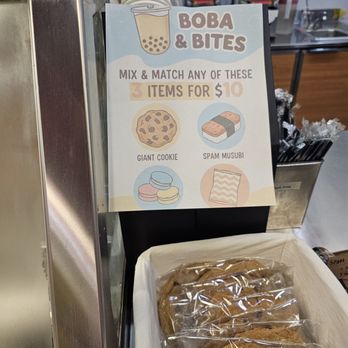 Yin Yang Tea - 3 for $10 deal - A promotional sign offers a deal for boba and bites, featuring illustrations of a cookie, sushi musubi, and macarons, with a basket of packaged cookies below. - Bubble Tea Near Me - Pasadena, California