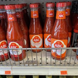 Items on display reflecting different prices. - The image shows several bottles of ABC Original Chili Sauce arranged on a store shelf. The bottles have red caps and labels with the ABC logo and the product name. The shelf has a metal wire design, and the price tag below indicates a cost of $2.79. The background includes other condiment bottles, but the focus is on the chili sauce bottles.