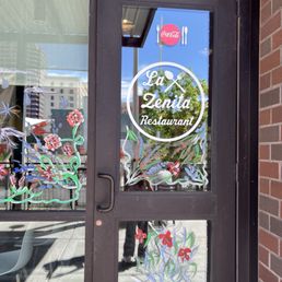 The entrance door of La Zenita Restaurant has floral window decals and displays the restaurant's name and logo.