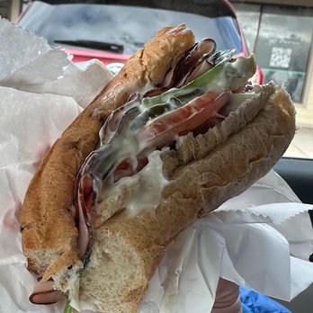 Subway - "Light mayo" - A close-up of a sandwich featuring shrimp, slices of ham, fresh lettuce, and mayonnaise, all inside a crusty baguette. The sandwich is held in front of a car window, with a red vehicle visible in the background. The sandwich is wrapped in white paper, emphasizing its fresh ingredients and casual presentation. - Sandwiches Near Me - Madison, Wisconsin