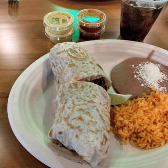Taco Pros - Barbacoa burrito combo - A Mexican meal featuring a burrito, Mexican rice, refried beans with cheese, and a lime wedge, served on a white plate with sauces and a soda in the background. - Mexican Near Me - Niles, Illinois
