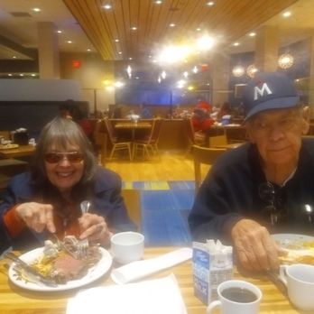 Tradewinds Buffet - Bonnie and George enjoying the prime rib at Tradewinds Buffet - A woman with sunglasses and an elderly man are seated at a restaurant table, eating food and drinking coffee, with other diners visible in the background. - Buffets Near Me - Welch, Minnesota