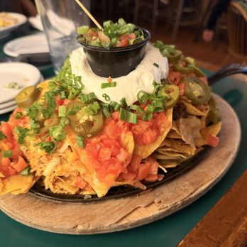 Red Lion - Red Lyon Nachos with chicken and beef - A serving of nachos with chips, melted cheese, diced tomatoes, jalapeños, green onions, and sour cream on top, served on a wooden platter. - Bars Near Me - Vail, Colorado