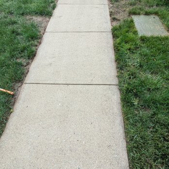 Cincy Wizard Washing - Sidewalk: you can see before and after clearly - Concrete sidewalk with cracks and uneven sections runs through a grassy residential area, with a parked car visible in the background. - Pressure Washers Near Me - Cleves, Ohio