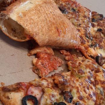 Hambone's Pizza - A slice of pizza with black olives, cheese, and toppings is placed inside a cardboard pizza box. Next to it, there is a calzone with a golden-brown crust. The pizza appears to have a variety of toppings, including cheese and olives, and the calzone is partially open, showing some filling. The box is on a wooden surface, and the image captures the food items from a close-up perspective. - Pizza Near Me - Cheyenne, Wyoming