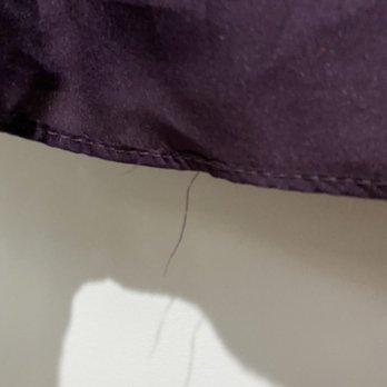 Kam's Alterations - Threads hanging loose - The image depicts a close-up view of purple fabric, likely part of a garment, with visible loose threads hanging from the hem area. The fabric appears to be slightly wrinkled, and the loose threads suggest it may require sewing or alteration. The background is a plain, light-colored surface. - Sewing & Alterations Near Me - Phoenix, Arizona