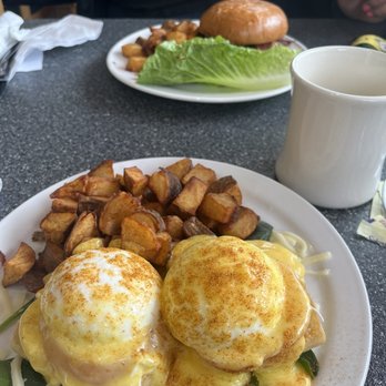 Studio One Cafe - The big East - Two plates of breakfast dishes, one with eggs Benedict and roasted potatoes, and another with a burger and lettuce, are on a table. - Breakfast & Brunch Near Me - Eugene, Oregon