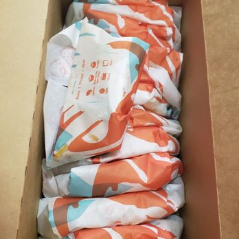 Taco Bell - Party Box of Tacos!! - A rectangular cardboard box contains multiple wrapped food items, possibly tacos, with orange, white, and blue wrapping paper, arranged in a single layer. - Fast Food Near Me - Hackettstown, New Jersey