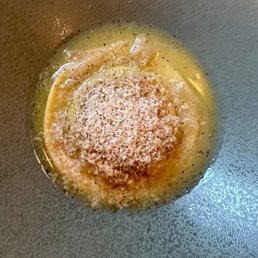 Egg Yolk Raviolo - Egg yolk raviolo with grated cheese on top, cooked in a pan, with a yellowish sauce surrounding it.