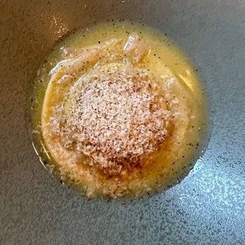 Margot - Egg yolk raviolo - Egg yolk raviolo with grated cheese on top, cooked in a pan, with a yellowish sauce surrounding it. - New American Near Me - Brooklyn, New York